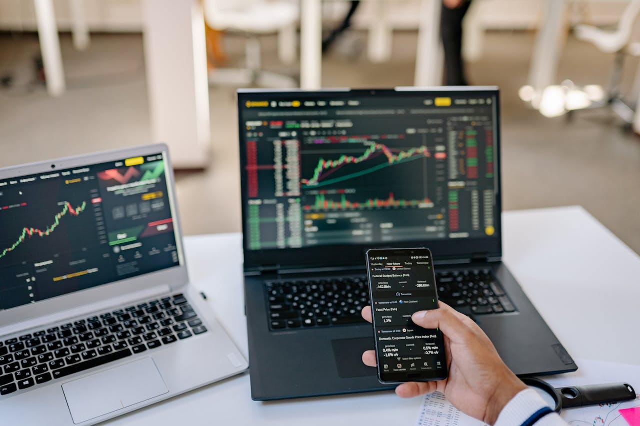services-03 A professional tracks stock market trends using two laptops and a smartphone, showcasing digital finance tools.